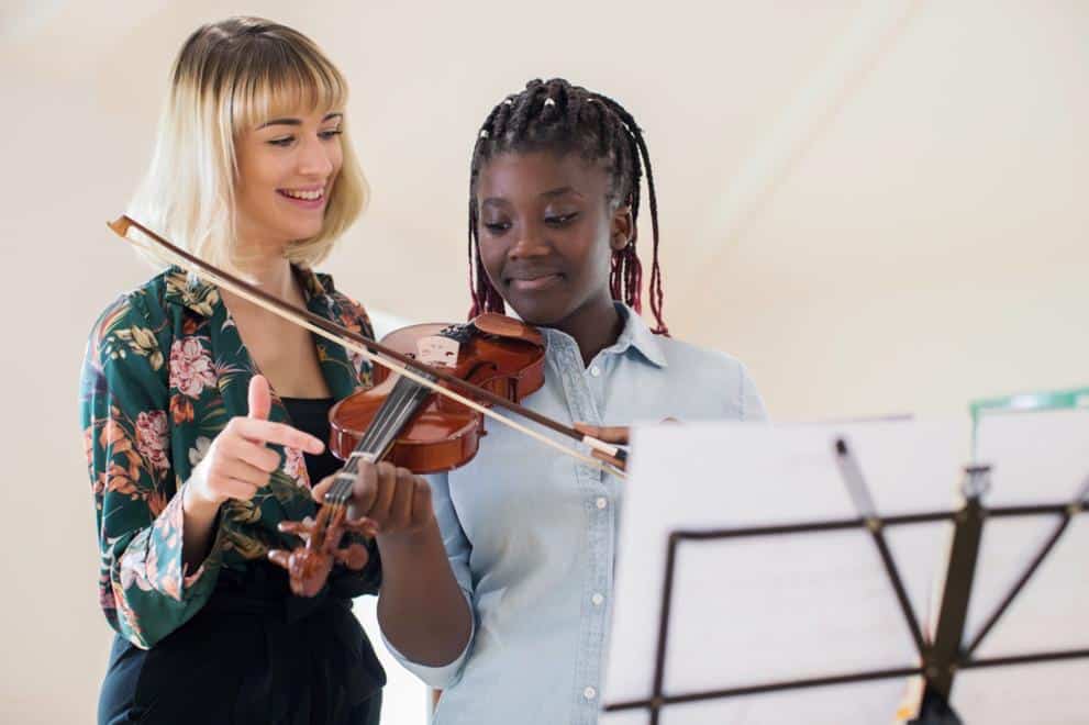 Music student playing a violin whist her teacher instructs her